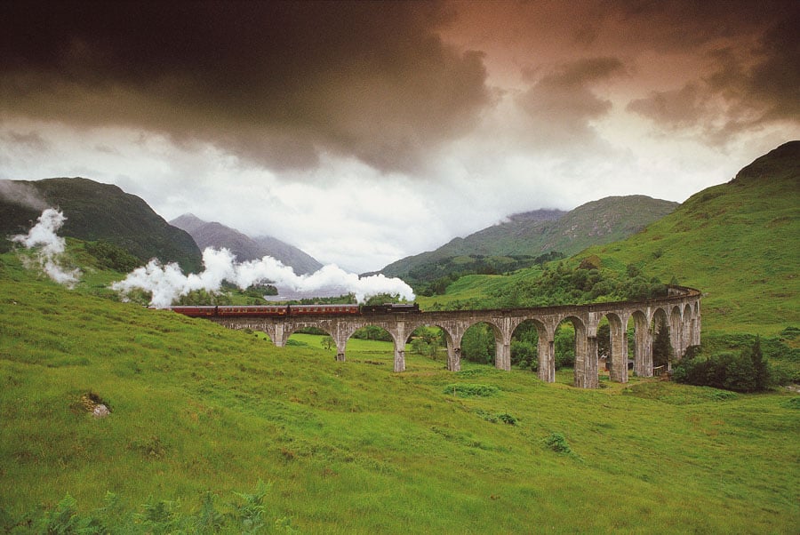 A STEAM TRAIN ON THE WEST HIGHLAND LINE CROSSES THE VIADUCT SPANNING GLEN FINNAN, AS IT APPROACHES THE VILLAGE OF GLENFINNAN, WITH LOCH SHIEL VISIBLE BEHIND, HIGHLAND.